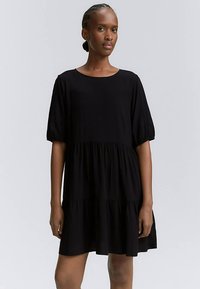 Must kleit, millel on lühikesed puffsääred, ümmargune kaelus ja kihiline disain lõdva istuvusega. Valmistatud pehmest, hingavast materjalist.