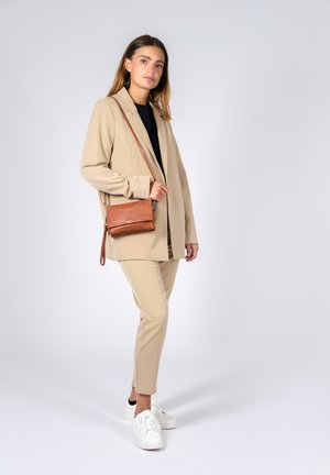 Blazer beige e pantaloni coordinati, abbinati a un top nero e scarpe da ginnastica bianche. Una borsa a tracolla in pelle marrone completa il look.
