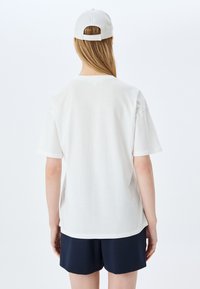 Hvid bomulds T-shirt med afslappet pasform, der har korte ærmer og rund halsudskæring. Sammen med navy farvede shorts og en matchende cap.