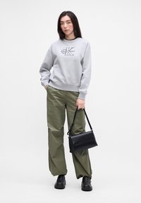 Γκρι φούτερ με μαύρο λογότυπο, ελαιόχροες φαρδιές παντελόνες και μαύρες μπαλέτες με πλατφόρμα. Το μοντέλο κρατάει μια μαύρη τσάντα χιαστί.