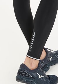 Zwarte sportleggings met reflecterende streepdetails, gecombineerd met donkerblauwe hardloopschoenen met een bovenwerk van mesh en een gevoerde zool.