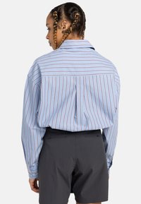 Striped shirt in light blue with narrow red lines, featuring a classic collar and buttoned cuffs, paired with dark grey shorts.