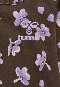 Brun tyg med blommönster i nyanser av lila. Har "hummel"-logotypen i vitt centrerad på designen.