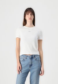 Tricou alb cu mânecă scurtă, cu o textură ribbed și logo-ul brodat "GAP" pe piept, asortat cu blugi din denim de un albastru deschis.