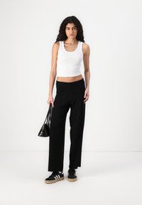 Black wide-leg pants, white ribbed tank top, black low-top sneakers with white stripes, and a small black handbag. Simple, casual outfit.