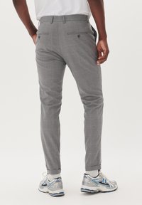 Pantalones de cuadros grises con un corte ajustado, que presentan dos bolsillos traseros con botones. Con dobladillos y combinados con zapatillas deportivas.