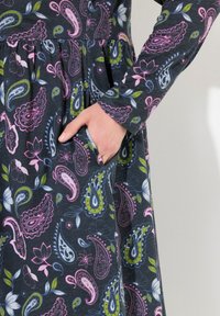 Långärmad klänning i mörk tyg med paisley- och blommönster i rosa, grönt och blått, med detalj av sidoficka.