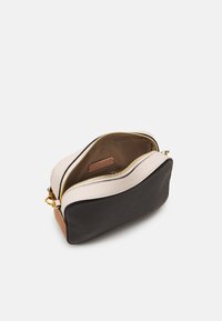 Borsa a pochette in pelle con parte superiore color crema, frontale nero e parte inferiore color beige. Zip dorata e interni beige con un'etichetta visibile.
