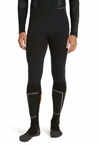 Leggings térmicos negros fabricados con una mezcla de tejidos de textura suave. Presentan detalles en naranja y gris en la parte inferior de las piernas. La cinturilla muestra el logo "FALKE".