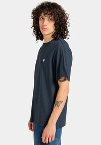 Granatowa bawełniana koszulka z okrągłym dekoltem, z krótkim rękawem i małym haftowanym logo na piersi. Gładka tekstura, luźny krój.