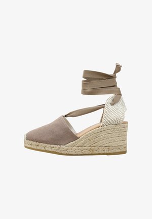 Alpargata de cuña beige con talón tejido, puntera cerrada de ante marrón, suela de cuerda trenzada y largas cintas para atar al tobillo.