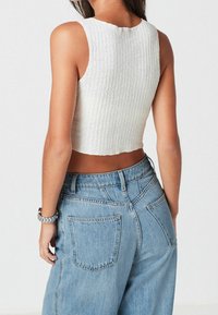 Biała prążkowana crop top z okrągłym dekoltem, zestawiona z jasnoniebieskimi dżinsami z wysokim stanem, które mają tylne kieszenie i luźny krój.