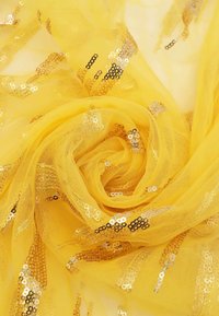 Tessuto di tulle giallo con paillettes dorate e argentate, disposto in una forma spirale fluida. Trama traslucida e leggera.