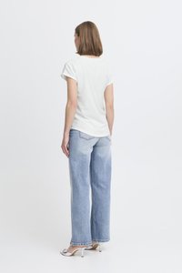 Balta, īsām piedurknēm t-kreklu, brīvā piegriezumā, kombinēta ar gaiši ziliem, platajiem džinsiem ar bālētu mazgāšanu un saplīsušiem malām. Vienkāršs dizains, minimālas detaļas.