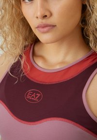 Αθλητική μπλούζα χωρίς μανίκια με μπορντό βάση και ροζ και κόκκινες λεπτομέρειες. Λείο υλικό, στρογγυλή λαιμόκοψη και επιβλητό λογότυπο EA7.