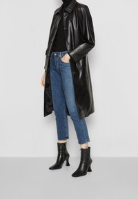 Svart läder trenchcoat med knappstängning, parat med blå denimjeans och svarta klackstövlar. Mjuk textur och skräddarsydd passform.