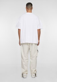 T-shirt bianca oversize con maniche corte e colletto tondo, abbinata a pantaloni beige a vestibilità ampia con tasche laterali e cerniere.