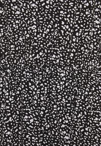 Czarna sukienka z tkaniny z białym nakropkowanym wzorem, z marszczonymi detalami w okolicy talii i gładką, lekką teksturą.