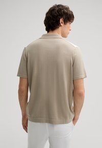 Beige short-sleeve polo shirt with a soft texture and plain design. Features a classic collar and a straight hemline.
