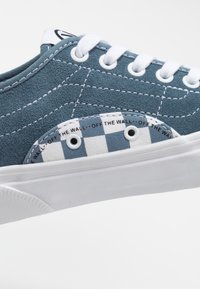 Baskets en daim bleu avec des lacets blancs, panneau latéral à damier et inscription "OFF THE WALL" le long du bord du panneau.