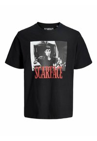 Sort bomulds t-shirt med et fremtrædende hvidt grafisk billede af en mand i en stol. Ordet "SCARFACE" er trykt i fed rød nedenfor billedet.