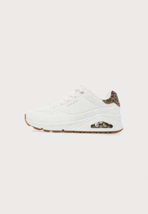 Άσπρο αθλητικό παπούτσι Skechers με σόλα με αερόφουσκες, σχεδιασμό με κορδόνια, καφέ λαστιχένια εξωτερική σόλα και λεπτομέρεια με μοτίβο λεοπάρδαλης στον γιακά της φτέρνας.