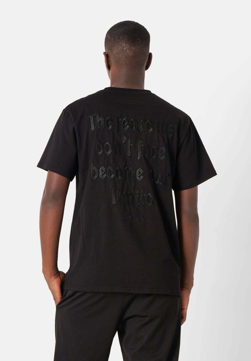 Zwarte katoenen t-shirt met grote reliëftekst op de achterkant en een relaxte pasvorm. Het ontwerp heeft een minimalistische stijl en een ronde halslijn.