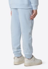 Pantalones de chándal azul claro en suave forro polar con un ajuste relajado, con puños elásticos y bolsillos laterales, combinados con zapatillas blancas.