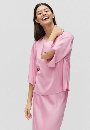 Lyserød bluse med brede ærmer og en afslappet pasform, lavet af glat materiale. Har et lagdelt design og sideslids.