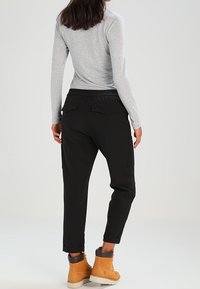 Svarta cargobyxor med sidofickor, ankelfållar och elastisk midja. Kombinerat med en långärmad grå topp och bruna stövlar.