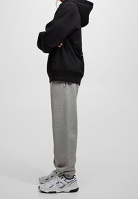 Zwarte hoodie met kangoeroezak, gecombineerd met grijze joggingbroeken. Schoeisel heeft een wit en zwart ontwerp. Eenvoudige, ontspannen silhouet.