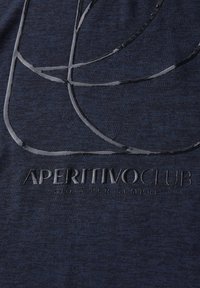 Námořnická modrá látka s hladkým povrchem, která má lesklý abstraktní vzor a text "APERITIVO CLUB" embosovaný ve spodní části.