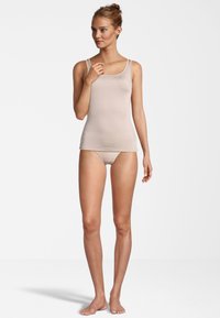Top in beige senza maniche con spalline sottili, silhouette aderente, texture liscia e design minimale. Abbinato a slip coordinati discreti.