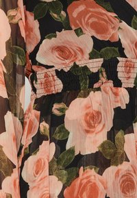 Schwarzes Kleid mit einem Blumenmuster, das große rosa Rosen und grüne Blätter zeigt. Der Stoff ist durchsichtig und hat einen gerafften Bund.