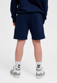 Marineblauwe shorts van zacht materiaal, met een eenvoudig ontwerp en een rechte snit. Gecombineerd met hoge sneakers en witte sokken.
