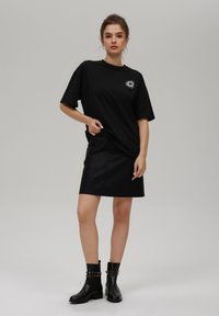 Crna oversized majica s grafikom sunca, uparena s crnom kožnom mini suknjom i crnim gležnjačama s dekorativnim hardverom.
