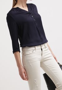 Marinblus med V-hals och trekvartsärmar, med en framknäppning, tillsammans med vita slitna slim fit-jeans.