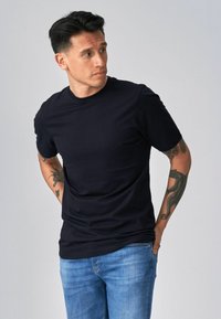 Tumši zila kokvilnas T-krekls ar apaļu kakla izgriezumu un īsām piedurknēm, apvienots ar gaiši zilām denim biksēm. Gluda tekstūra, minimāls dizains.