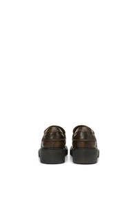 Een paar donkerbruine leren loafers met dikke zwarte zolen, gefotografeerd van achteren op een witte achtergrond.