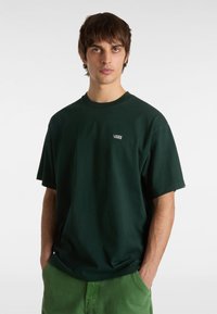 Tmavě zelené bavlněné tričko s kulatým výstřihem a krátkými rukávy, na levé straně hrudi se nachází malé bílé logo "VANS".
