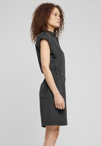 Robe noire à manches courtes avec col, taille élastique et deux poches latérales ; texture lisse et design jusqu'aux genoux.