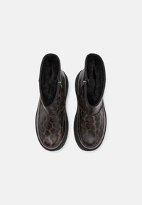 Paire de bottines montantes à la cheville avec motif léopard foncé, doublure en fourrure noire et fermetures éclair latérales, vues de dessus sur un fond blanc.