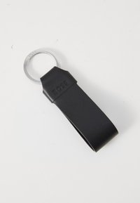 Zwarte leren sleutelhanger met een gladde textuur, voorzien van een zilveren metalen ring en een reliëf merknaam. Eenvoudig, rechthoekig ontwerp.