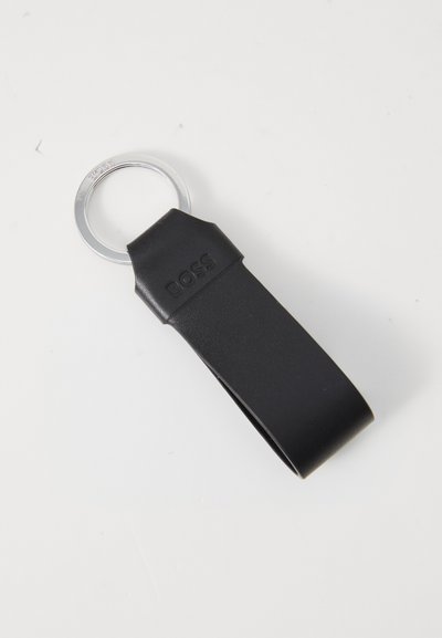 Porte-clés en cuir noir avec une texture lisse, doté d'un anneau en métal argenté et d'un nom de marque en relief. Design simple et rectangulaire.