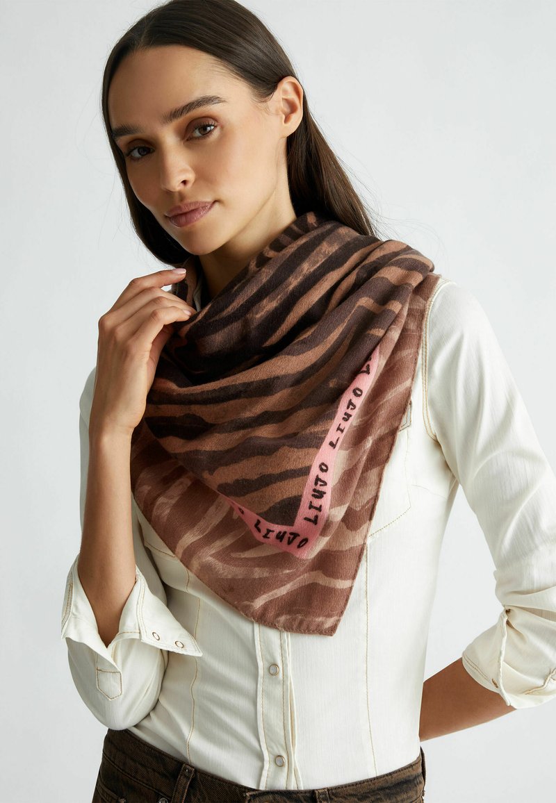 Sciarpa marrone e rosa con motivo, realizzata in tessuto morbido, caratterizzata da un design a zigzag e testo del marchio sul bordo, indossata sciolta attorno al collo.