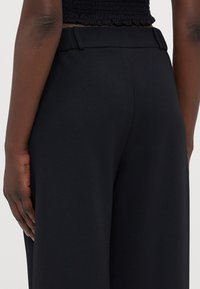 Black wide-leg pants with a smooth texture. Features a high waistband with belt loops. Back view shows clean lines and tailored design.