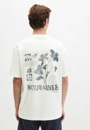 Person wearing white t-shirt with black floral and bee prints and text about nature on the back.