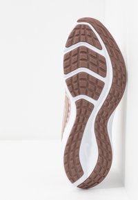 Semelle de chaussure de sport avec un motif en caoutchouc marron texturé, présentant une semelle intermédiaire blanche et des bords lisses. Tread visible pour l'adh�érence.