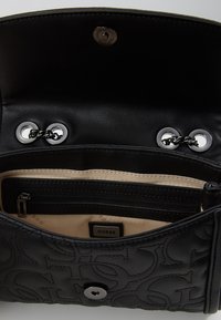 Black leather handbag with embossed logo pattern, interior features a cream lining, zippered compartment, and silver hardware accents.