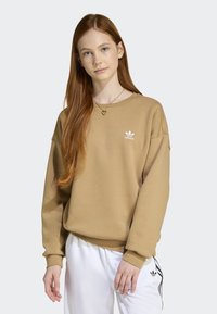 Beige sweatshirt med rund halsringning och vitt Adidas-logotyp på bröstet. Blusen har långa, något överdimensionerade ärmar och ribbade muddar.